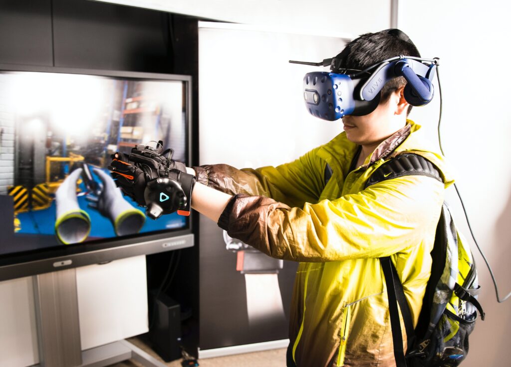 Man in yellow jacket wearing a VR headset and gloves, appearing to play a video game.